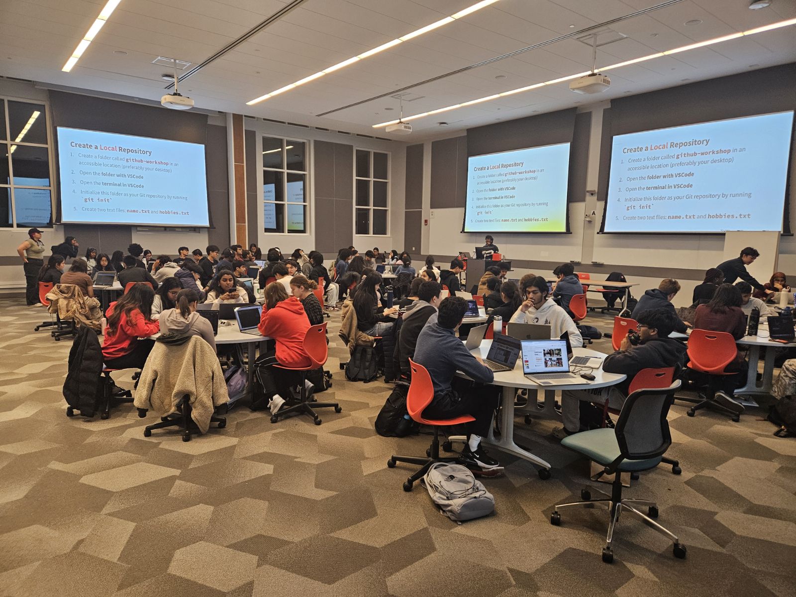 Room of students seated at circular tables with screens showing a presentation during a workshop
