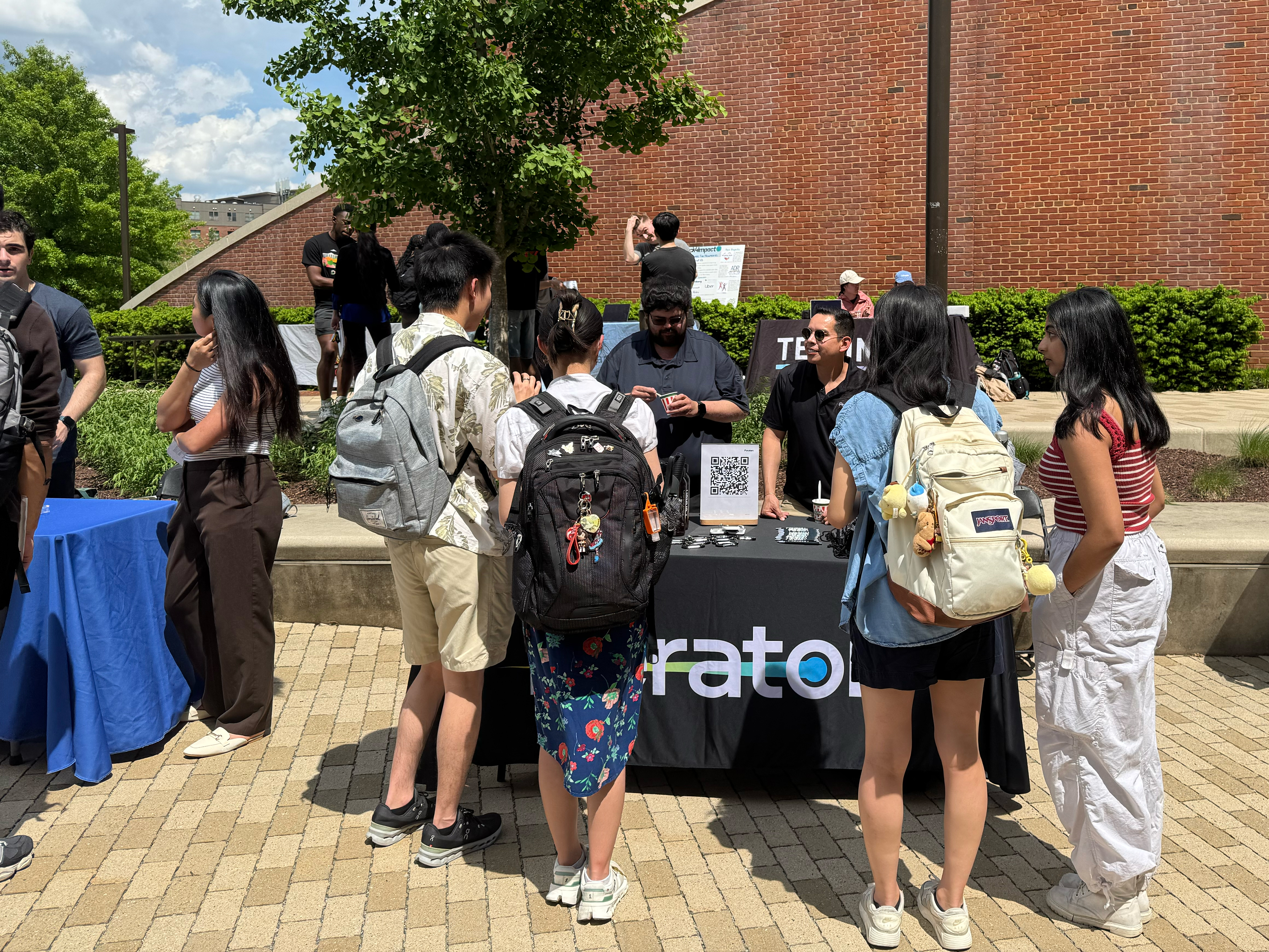 A group of students gathers around the Peraton partner table in the Iribe Center Courtyard