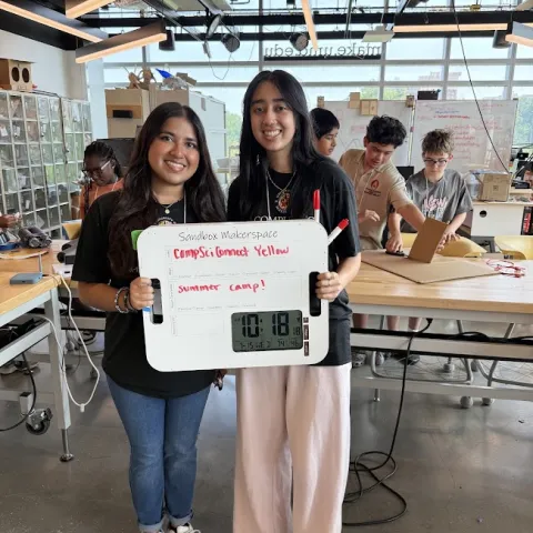 Two students holding a sign with a clock