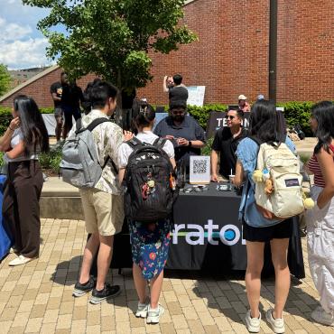 A group of students gathers around the Peraton partner table in the Iribe Center Courtyard