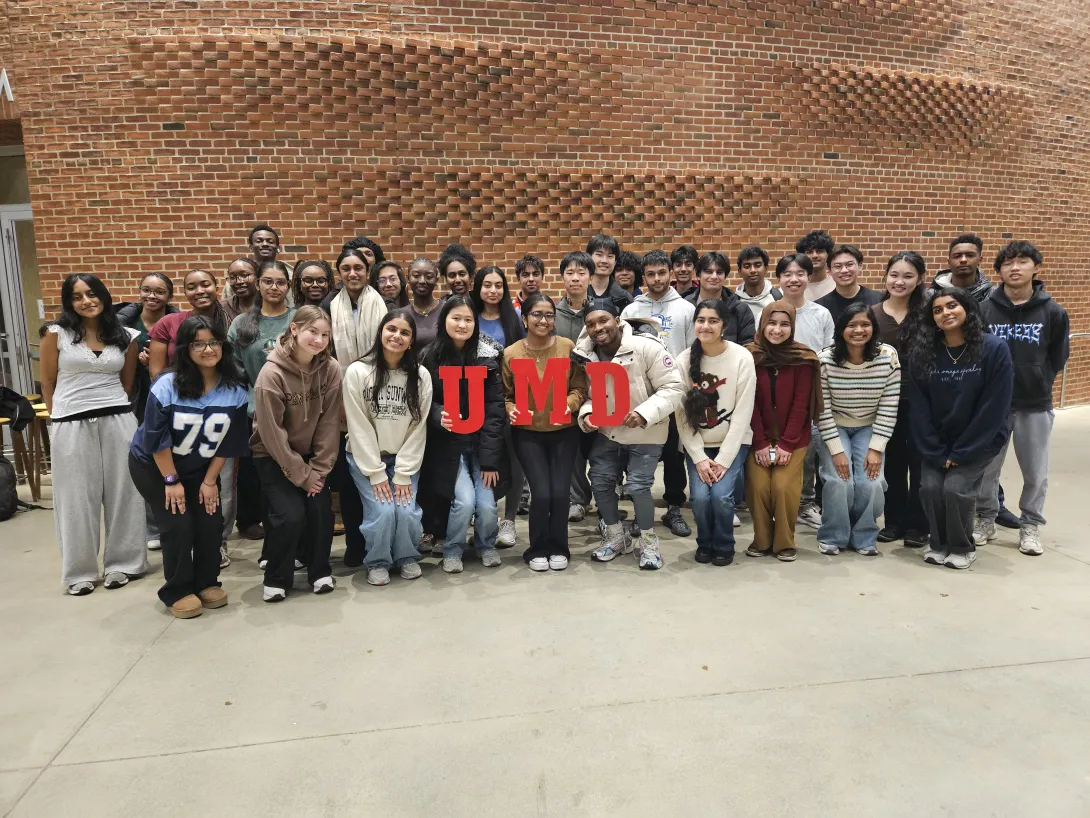 Large group of students posing in front of a brick wall holding up red letters "UMD"