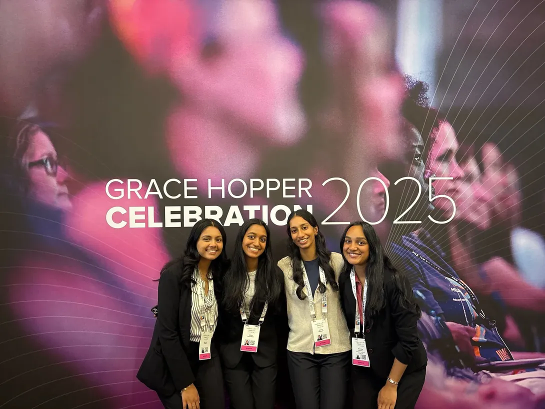 Group of four students in front of the 2025 Grace Hopper Celebration banner