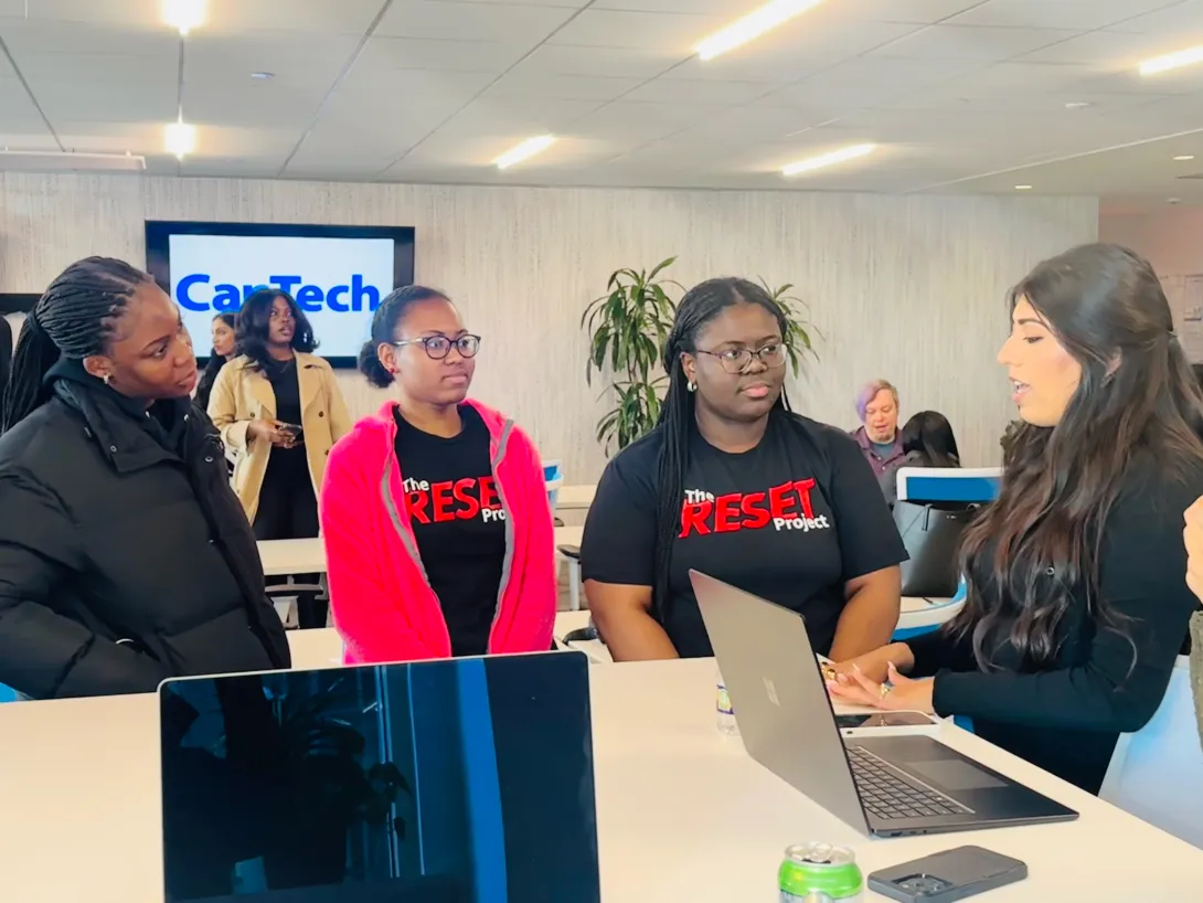 RESET Scholars network with a CapTech employee at a table with laptops in front of a screen with the CapTech logo