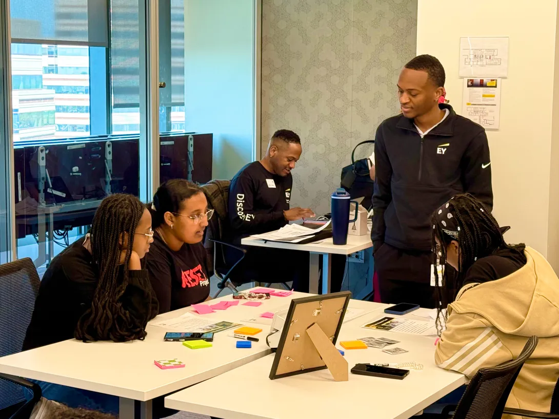 A group of RESET Scholars seated at a table while talking with an EY employee, who is standing on the right